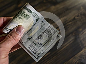 Close up of male hand holds two banknotes of hundred dollars on a wooden background. new hundred-dollar bills.Money USA dollar