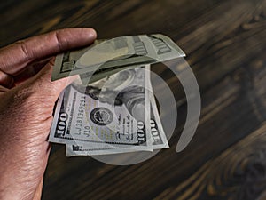 Close up of male hand holds two banknotes of hundred dollars on a wooden background. new hundred-dollar bills.Money USA dollar