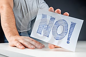 Close-up male hand holds a white card with the word no. Failure disagreement protest