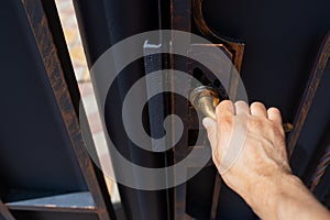 Close-up of male hand opens the metal outdoor gates. Door handle