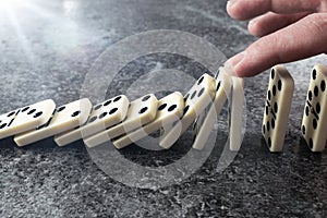 Close-up of male hand preventing line of domino tiles from toppling and falling