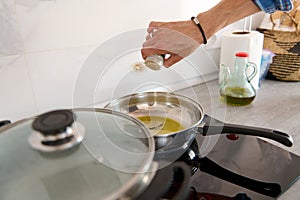 Close-up male hand seasoning dish, putting pepper into a pan with bay leaf and olive oil frying on stove, cooking dinner