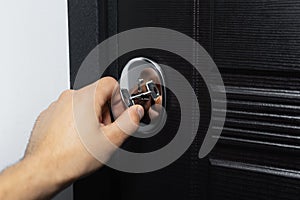 Close-up of male hand unlocking or locking lock of modern house door with key.