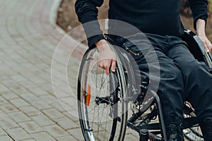 Close-up of male hand on wheel of wheelchair during walk in park