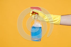 Close up of male hand in yellow gloves click on spray bottle with cleaner liquid with place for text isolated on yellow