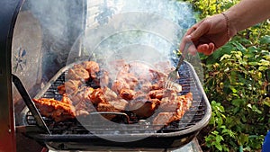 Close up of male hands baking meal outdoors at grill using a fork to turning around meat for not burn out. Barbeque and picnic sea