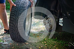 Close up of male hands changing car tire outside. Replacing broken vehicle tire on the grass. Travel accident