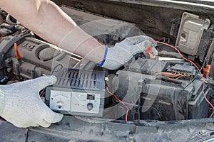 Close-up of male hands checking voltage of automobile battery under hood machine with accuracy. Automotive checkup concept