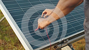 Close up of male hands checking voltage in solar panels with multimeter outdoors. Competente energy technician