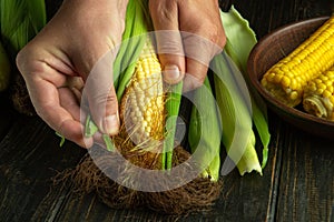 Close-up of male hands cleaning head of corn from green husk before cooking