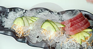 Close-up male hands of a cook in gloves laying out pieces of fresh fish and vegetables on a substrate of ice on a plate