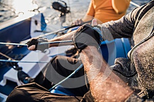 Close-up of male hands in gloves pulling rope of sailboat while mooring yacht and sitting with friends on deck.