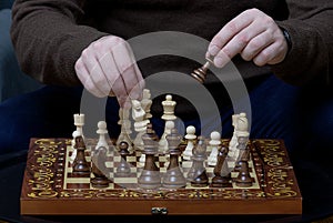 Close-up of male hands holding a chess piece above other pieces on a wooden chessboard.