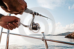 Close up of male hands holding fishing rod while fishing on sailboat in open sea