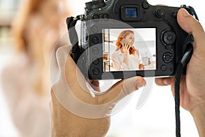 Close up of male hands holding a professional DSLR camera and taking a shot of young red haired woman.