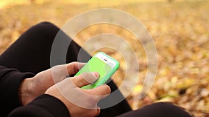 Close up male hands are holding smartphone with green screen on a background of autumn leaves, press browsing chroma key