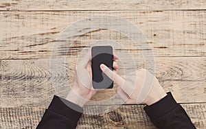 Close up of male hands holding smartphone and pointing finger to graph and text on screen at table wooden planks. Hipster style. T