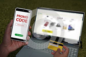 Close up of male hands holding smartphone with red written words Promo code on the screen and credit card on blur laptop