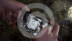 Close up of male hands holding smartphone and taking pictures of a clean water and stones. Clip. Cold clean spring water