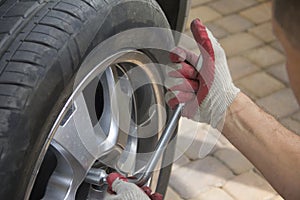 Close-up of male hands holding a wheel wrench on the background of a car wheel. The key is in the hand of an auto