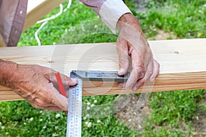 Close-up of male hands holding woodworking marking tool - red pencil and metal ruler on a background of green grass on a summer