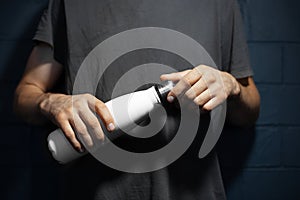 Close-up of male hands, openes steel thermo water bottle of white color, on the background of black brick wall. photo