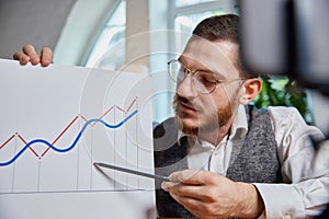 Close up male hands with pen pointing on business chart and mobile phone. People working with charts. Stock market