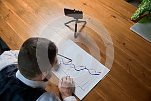 Close up male hands with pen pointing on business chart and mobile phone. People working with charts. Stock market