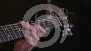 Close up of male hands playing acoustic guitar with capo on dark background.