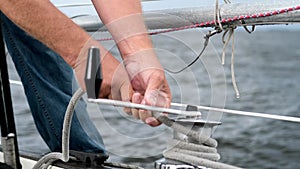 Close up of male hands pulling rope of sailboat, Yachtsman hands dealing with yacht ropes on halyard winch, Rope hauling