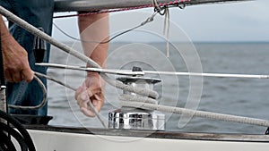 Close up of male hands pulling rope of sailboat, Yachtsman hands dealing with yacht ropes on halyard winch, Rope hauling