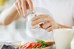 Close up of male hands seasoning food by salt mill