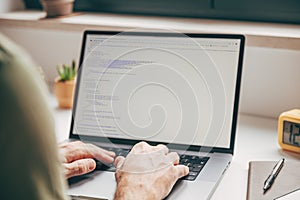 Close-up of male hands typing code on laptop computer at home office, concept of programming, software development, and remote
