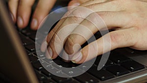 Close up of male hands typing on laptop keyboard side view.