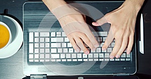 Close up of male hands typing on laptop keyboard at workplace. Top view