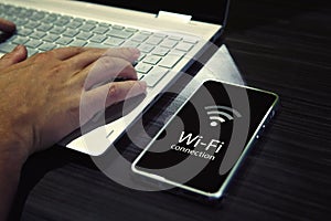 Close up of male hands typing on laptop keypad and checking the smartphone wi-fi connection. Cellphone with signal icon