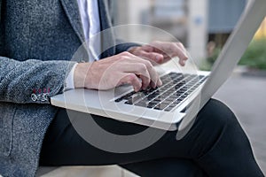 Close-up of male hands typing on laptop outside