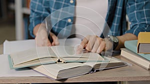 Close-up male hands unrecognizable young male student sitting in library doing homework preparing exam test writing