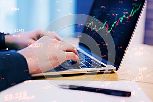 Close up of male hands using laptop with abstract candlestick forex graph and bid data numbers on blurry desktop background with