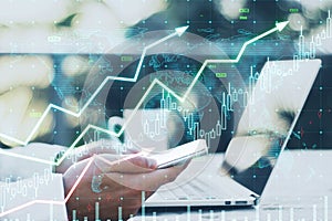 Close up of male hands using laptop and cellphone at desk with coffee cup and growing upward chart, map, arrows and forex graph on