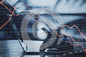 Close up of male hands using laptop computer keyboard and cellphone with glowing downward red forex chart on blurry outdoor