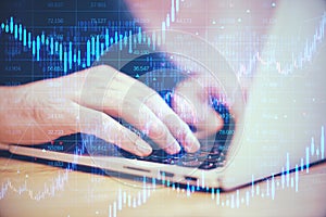 Close up of male hands using laptop keyboard with creative candlestick forex chart with index on blurry background. Trade, finance