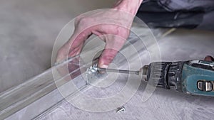 Close-up of male hands. A worker uses a cordless drill to drill a hole in a dark gray metal stick. Handyman drills