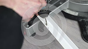 Close-up of male hands. A worker uses a cordless drill to drill a hole in a white plastic stick. The worker is drilling.