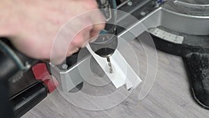 Close-up of male hands. A worker uses a cordless drill to drill a hole in a white plastic stick. The worker is drilling.