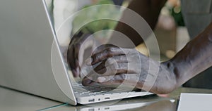 Close-up of male hands working with laptop computer typing while African American man managing flower shop