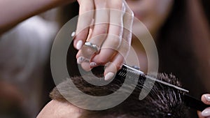 Close up of male head and hands of female hairstylist cutting hair ends of client using comb and sharp professional