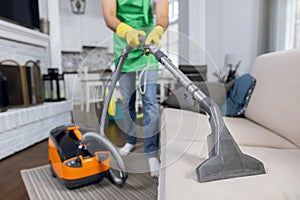 Close up of male janitor using vacuum cleaner for cleaning couch
