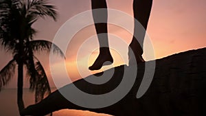 Close up of male legs. Young man walking on a palm tree at tropical beach during beautiful sunset. Slow motion. Travel