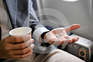 Close-up, A male passenger holding a cup of water and an airsick motion sickness pills